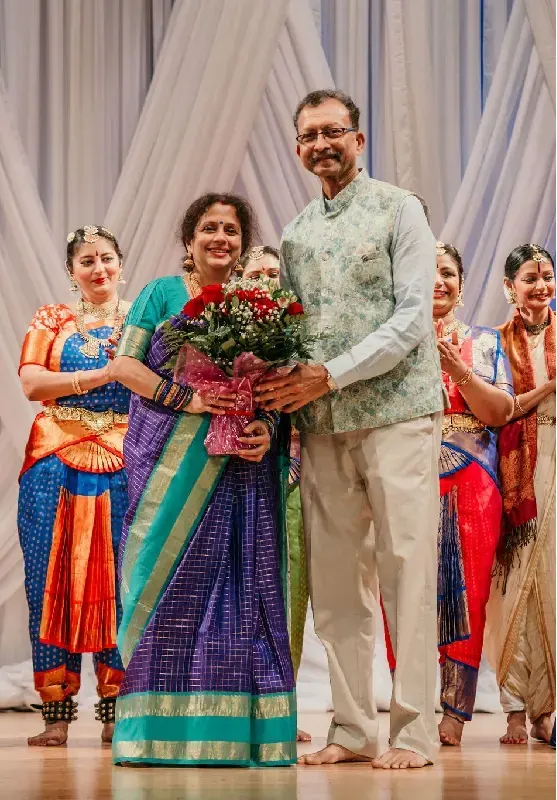Roopa Arts Cultural Center leadership being honoured on stage, flanked by dancers in Bharatanatyam costume, at the close of a production.